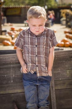 Frustrated Little Boy at Pumpkin Patch Farm Standing Against Old Wood Wagon.
