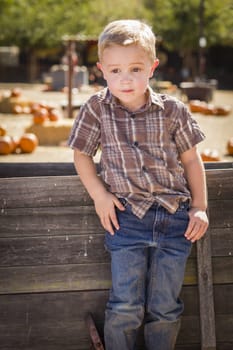 Adorable Little Boy at Pumpkin Patch With Hands in His Pockets Leaning on Antique Wood Wagon in Rustic Ranch Setting.
