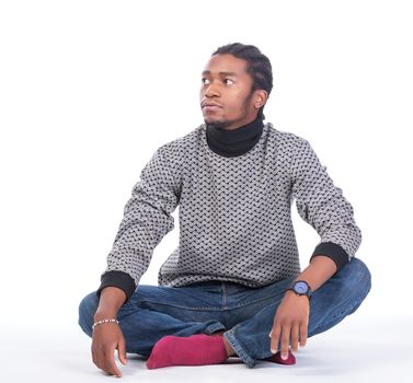 Young African-American male sitting on the ground looking to his side in a white background