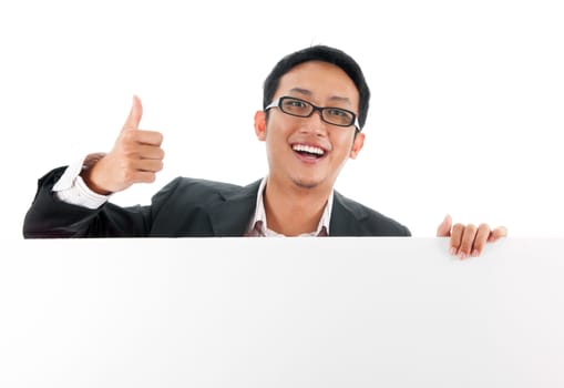 Blank paper for advertisement.  Young Asian executive male showing thumb up hand sign holding a white card board ready for text, isolated over white background.