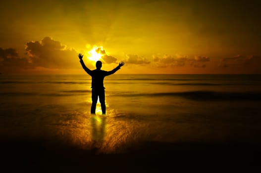 Silhouette of businessman standing in sea water  with natural golden sunlight at beach.