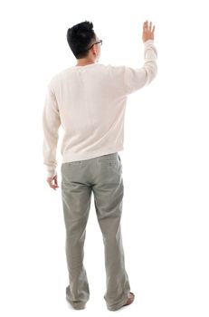 Rear view of Asian man hand touching on transparent virtual screen, space for text/button, full length standing isolated on white background.