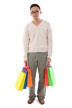Bored Asian man shopper holding shopping bags waiting for his girlfriend standing isolated over white background