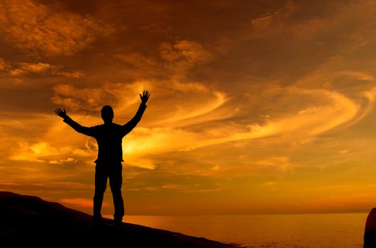 Silhouette of businessman standing on rock facing ocean open arms looking at the sky