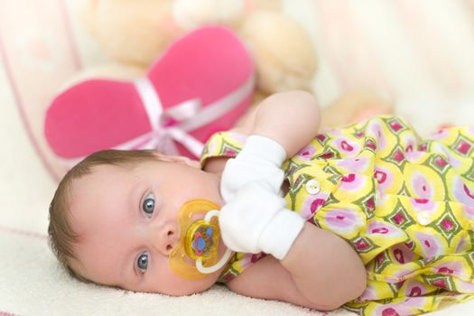 Infant baby girl (1 month old) lying on bed with teddy bear