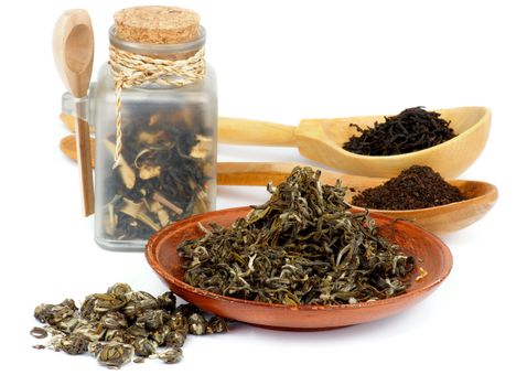 Arrangement of Various Black and Green Tea Leafs in Transparent Container, Wooden Spoons and Plate isolated on white background