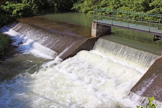 a dam retaining water from a swollen river with its bridge and waterfall