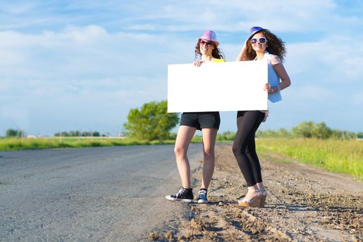 Two young women stand with a blank banner on the side of the road, place for text