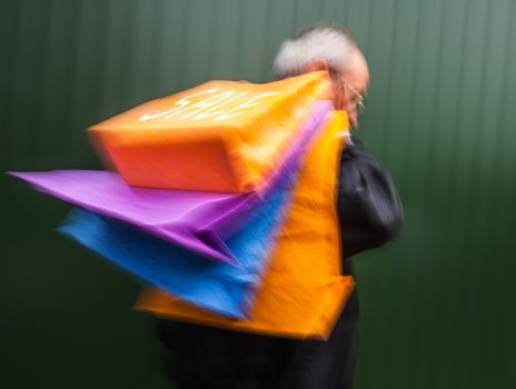 Holiday sales. An elderly man with many shopping bags in his hand. Intentional motion blur