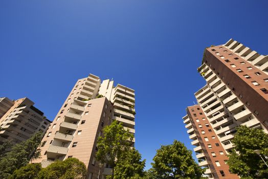 Three tall buildings with trees and blue sky
