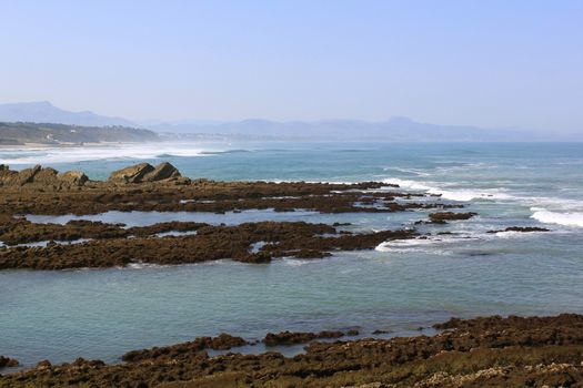 panoramic views of the ocean with its rocks and waves over a blue sky