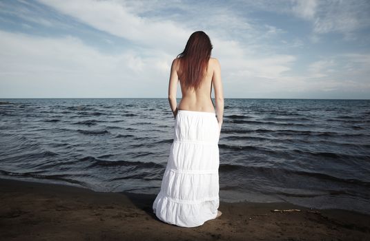 Rear view on the sad lady with long  hairs standing at the beach