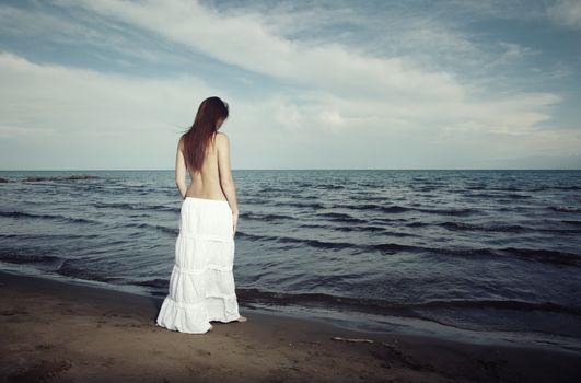Alone lady standing on the beach at the dark water of the sea. Horizontal rear view