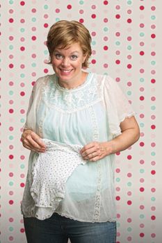 Excited pregnant woman holding up baby clothes