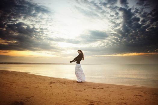 Single lady standing and walking along the beach during sunrise or sunset. Vivid colors