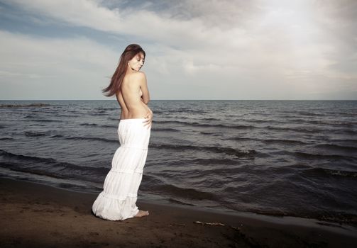 Topless lady with long hairs standing near the cold sea. Horizontal photo
