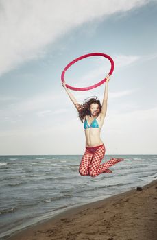 Active lady at the beach jumping with red hula hoop. Vertical photo