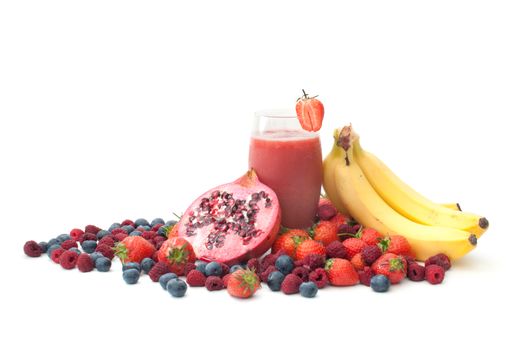 Fruit juice in a glass surrounded with pomegranate, strawberries, blueberries and raspberries 