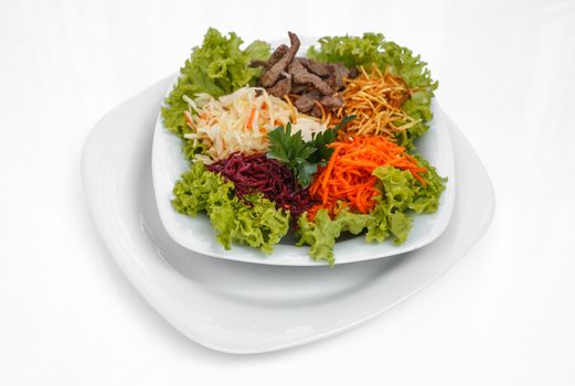 Fresh vegetable salad with slices of meat, filmed on a sheet of white plastic, close-up