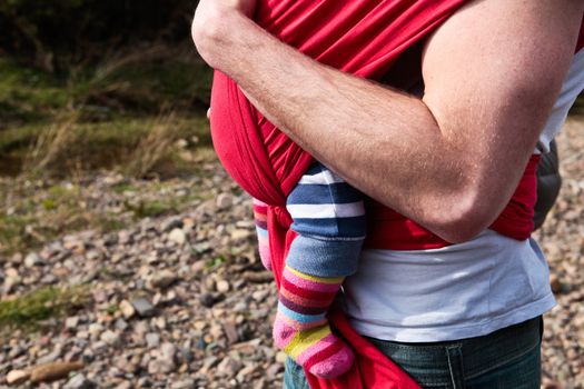 Young father carrying abbay girl in a carrier sling