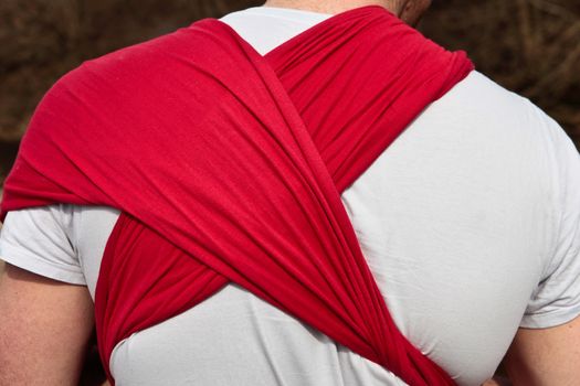 Red cloth baby sling on the back of a young father