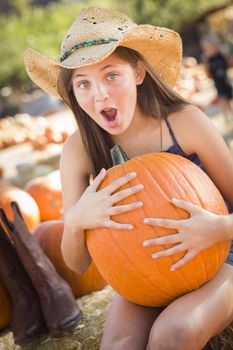 Preteen Girl Holding A Large Pumpkin at the Pumpkin Patch in a Rustic Setting.