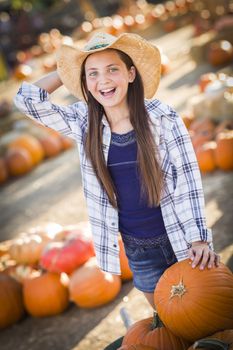 Preteen Girl Wearing Cowboy Hat Playing with a Wheelbarrow at the Pumpkin Patch in a Rustic Country Setting.
