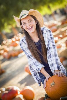 Preteen Girl Wearing Cowboy Hat Playing with a Wheelbarrow at the Pumpkin Patch in a Rustic Country Setting.
