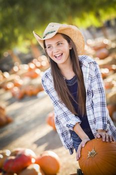 Preteen Girl Wearing Cowboy Hat Playing with a Wheelbarrow at the Pumpkin Patch in a Rustic Country Setting.
