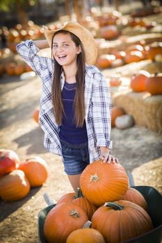 Preteen Girl Wearing Cowboy Hat Playing with a Wheelbarrow at the Pumpkin Patch in a Rustic Country Setting.
