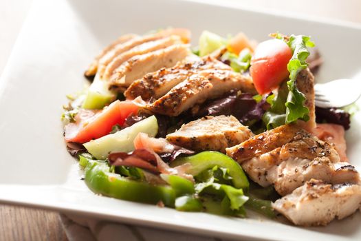 Freshly prepared grilled chicken chef style salad with tomato cucumber green pepper and romaine lettuce.