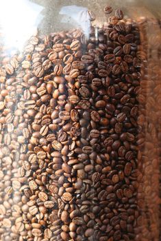 Brown coffee beans in glass container, close-up of coffee beans for background and texture