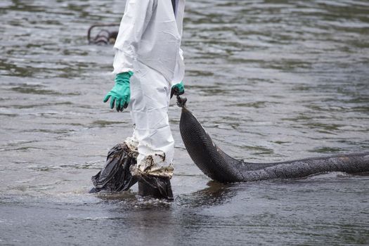 A Worker in biohazard suits hold a used Oil Containment boom as cleaning operations from a beach of Samet Island on July 31, 2013 in Rayong, Thailand.