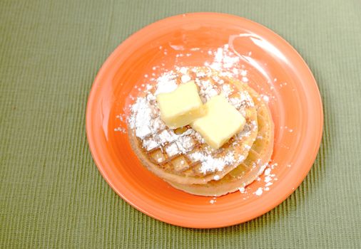 waffles with powdered sugar and butter on orange plate