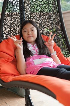 girl relaxing emotion on hanging bed at home terrace and show two finger victory sign