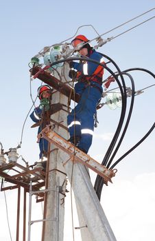 Electricians in blue overalls working at height on a support with a lot of wires and insulators