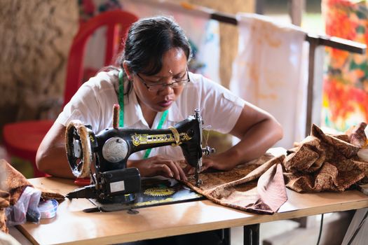 BALI, INDONESIA - Sep 21: Balinese female tailor sew on a machine on Sep 21, 2012 in Ubud, Bali, Indonesia. Ubud is popular region on Bali as area with handmade souvenirs. 