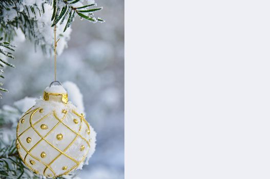 Christmas note with a snow covered ornament bulb hanging in a tre. Space for your text in very light blue color.