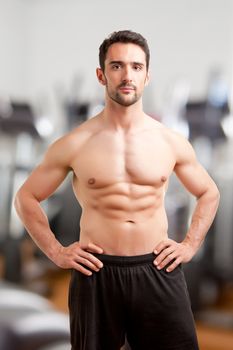 Fit man standing shirtless with his arms at his waist in a gym