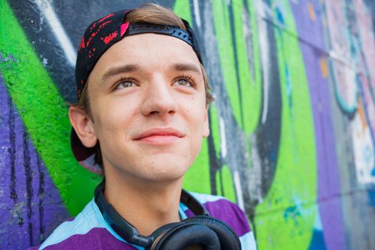 Close-up portrait of happy teens boy with headphones near painted wall listening to music