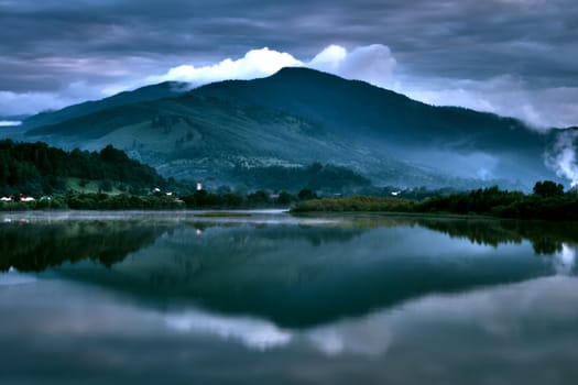 Beautiful blue reflection of the mountains in a perfectly still section of the lake below on a dark cloudy weather.