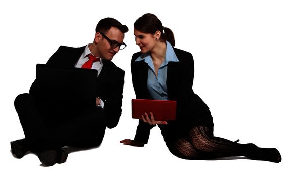 Young business couple sharing one another's work on their laptops while sitting against a white background.