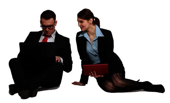Young business couple sharing one another's work on their laptops while sitting against a white background.