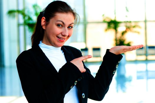 Happy young woman holding something on the palm of your hand and points a finger at her