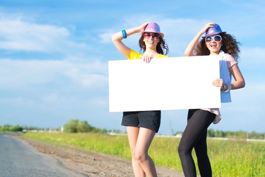 Two young women stand with a blank banner on the side of the road, place for text