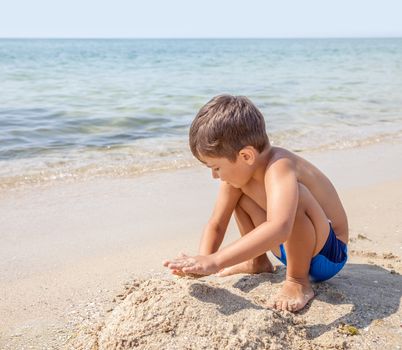 A caucasian child boy playing with sand in the beach