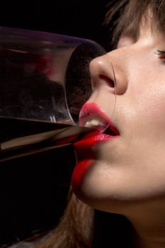 Closeup of the mouth and sexy red lips of a young woman drinking red wine from a wineglass against a dark background