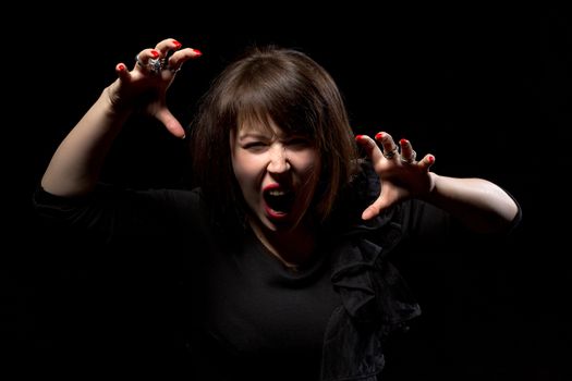 Woman throwing a temper tantrum screaming in anger and clawing the air with her hands on a dark background