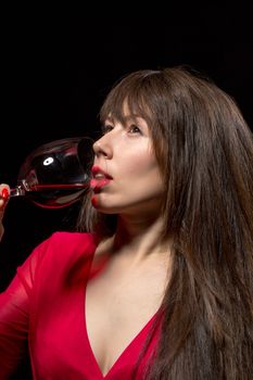 Young woman drinking red wine from a wineglass against a dark background