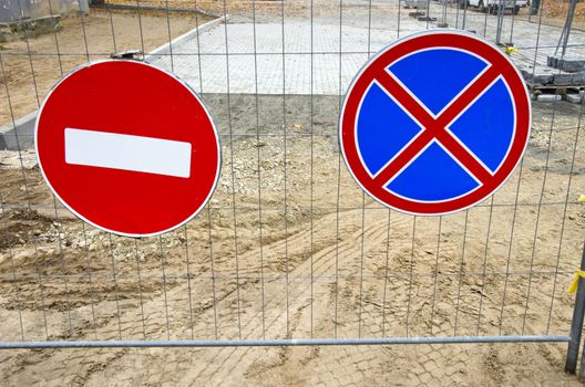 two road signs on street repair fence